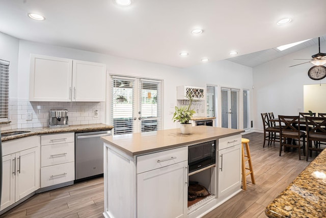 kitchen with dishwasher, white cabinetry, ceiling fan, and lofted ceiling with skylight