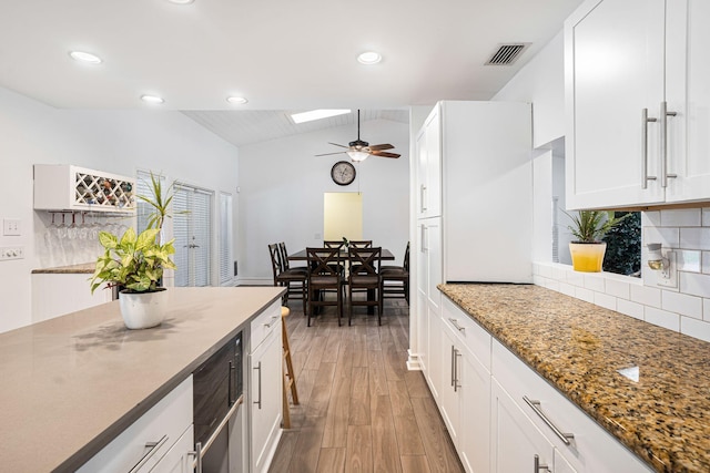 kitchen with white cabinets, ceiling fan, decorative backsplash, stone countertops, and light hardwood / wood-style floors