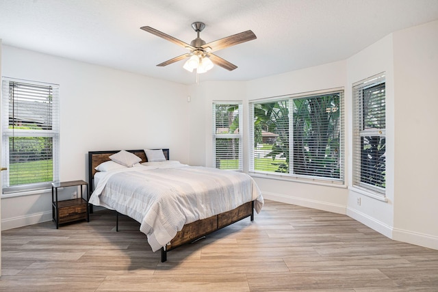 bedroom with multiple windows, light hardwood / wood-style floors, and ceiling fan