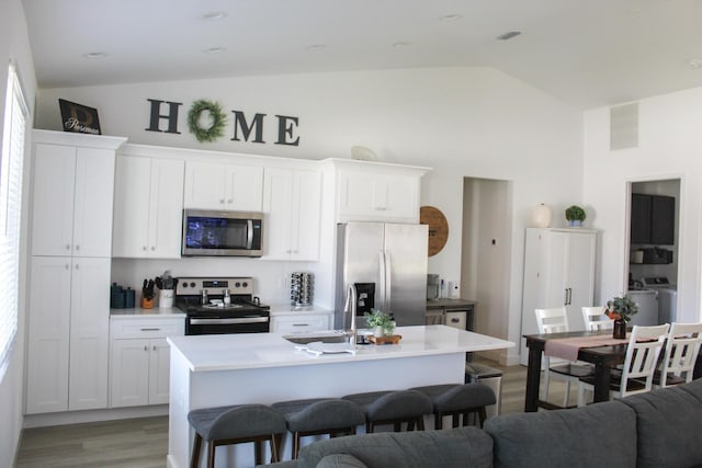 kitchen featuring white cabinets, lofted ceiling, a kitchen island with sink, and appliances with stainless steel finishes