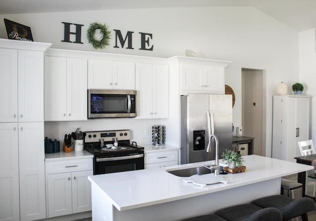 kitchen with appliances with stainless steel finishes, white cabinetry, lofted ceiling, and an island with sink