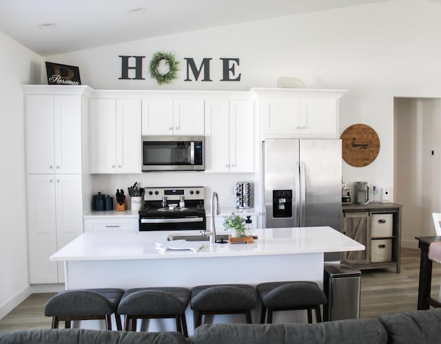 kitchen with appliances with stainless steel finishes, a center island with sink, white cabinetry, and lofted ceiling