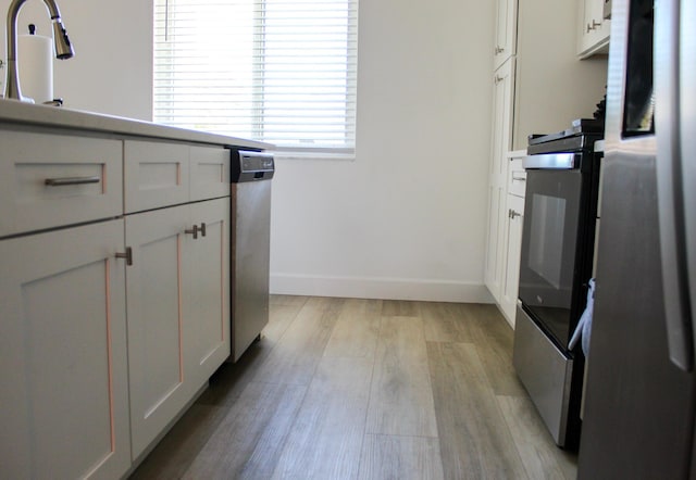 kitchen featuring oven, sink, stainless steel fridge, light hardwood / wood-style floors, and white cabinetry