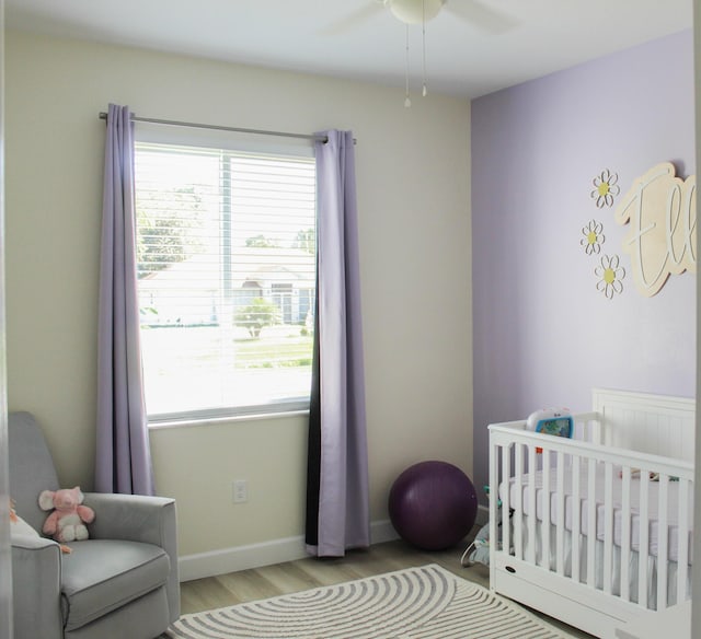 bedroom featuring ceiling fan, light wood-type flooring, and a nursery area