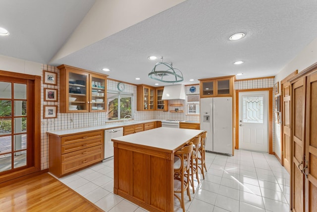 kitchen with light tile patterned floors, backsplash, white appliances, a kitchen island, and custom range hood