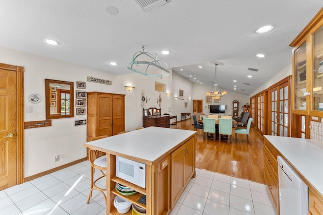 kitchen featuring white appliances, vaulted ceiling, light tile patterned floors, a kitchen island, and hanging light fixtures