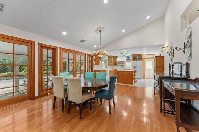 dining room with high vaulted ceiling, french doors, light hardwood / wood-style flooring, a textured ceiling, and a chandelier