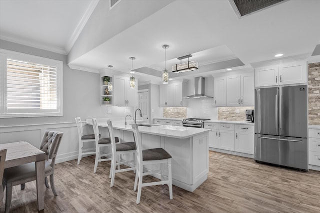 kitchen with stainless steel appliances, wall chimney exhaust hood, white cabinets, and hanging light fixtures