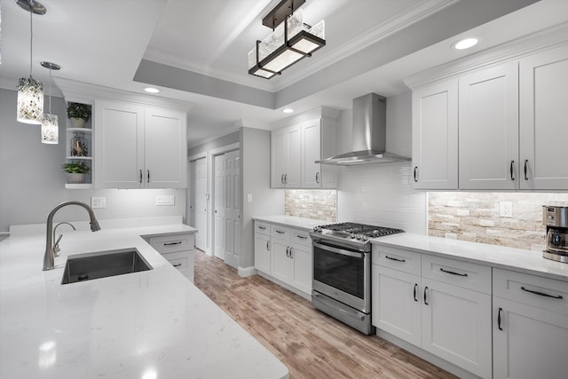 kitchen featuring stainless steel gas range, wall chimney exhaust hood, a tray ceiling, white cabinets, and sink