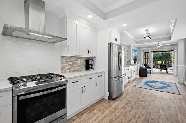 kitchen with stainless steel appliances, wall chimney range hood, backsplash, white cabinets, and ornamental molding