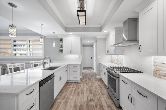 kitchen with sink, white cabinets, wall chimney range hood, pendant lighting, and appliances with stainless steel finishes