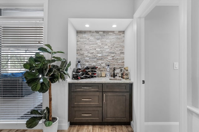 bar featuring light hardwood / wood-style floors, dark brown cabinets, and sink