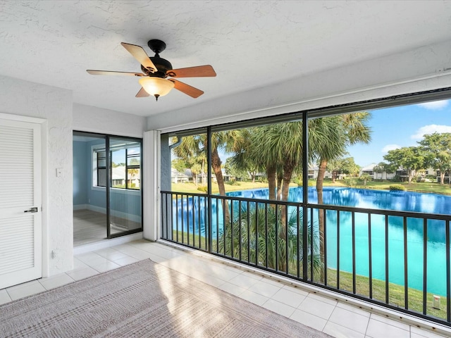 unfurnished sunroom featuring ceiling fan and a water view