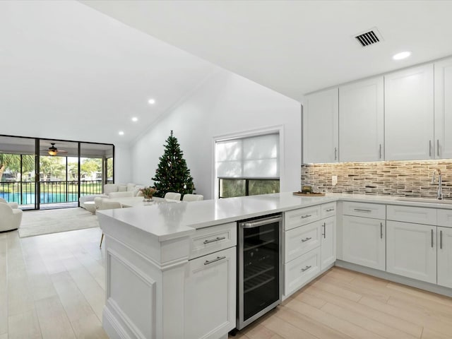 kitchen featuring kitchen peninsula, wine cooler, tasteful backsplash, sink, and white cabinetry