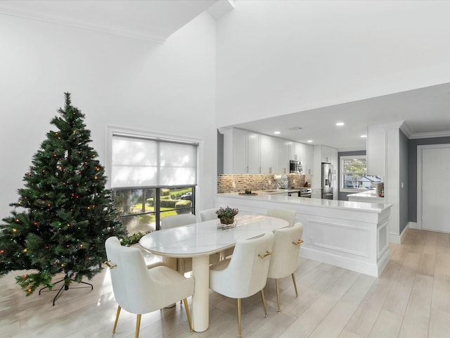 dining room with a high ceiling, light wood-type flooring, and crown molding