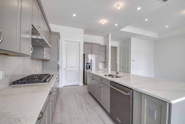 kitchen featuring stainless steel appliances, extractor fan, a tray ceiling, sink, and an island with sink