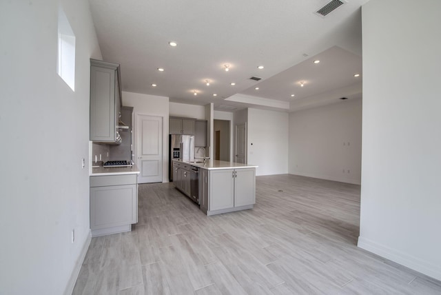 kitchen featuring light wood-type flooring, gray cabinetry, stainless steel appliances, sink, and a center island with sink