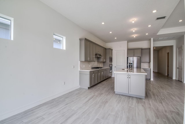 kitchen featuring gray cabinetry, decorative backsplash, range hood, a kitchen island with sink, and appliances with stainless steel finishes