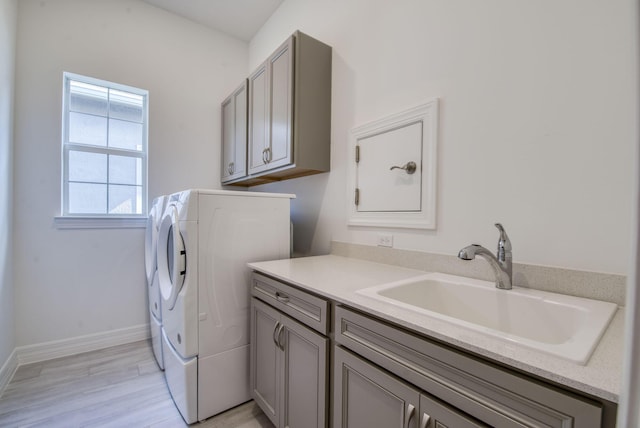 clothes washing area with cabinets, light wood-type flooring, washer and dryer, and sink