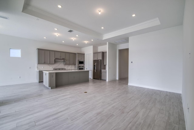 kitchen with backsplash, a kitchen island with sink, appliances with stainless steel finishes, and a tray ceiling