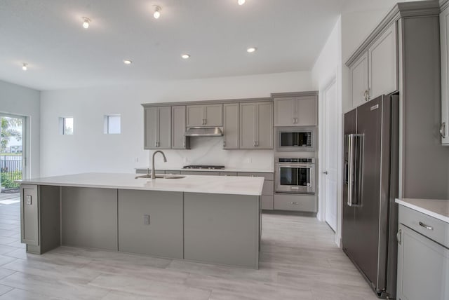 kitchen with gray cabinetry, a kitchen island with sink, sink, and appliances with stainless steel finishes