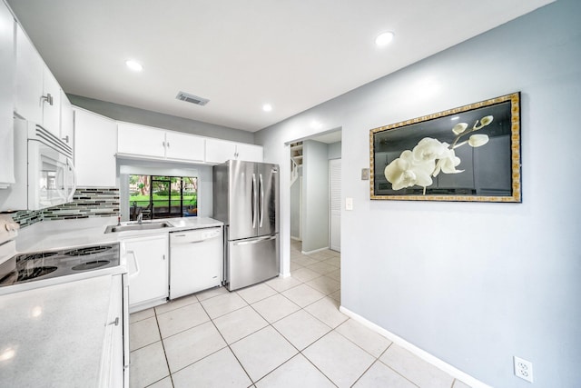 kitchen with tasteful backsplash, white appliances, sink, light tile patterned floors, and white cabinets