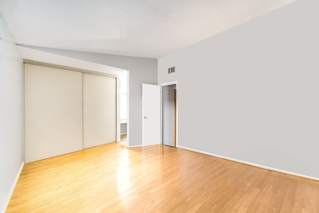 unfurnished bedroom featuring light wood-type flooring, a closet, and lofted ceiling