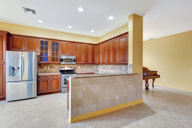 kitchen featuring light tile patterned floors, appliances with stainless steel finishes, light stone countertops, decorative backsplash, and kitchen peninsula