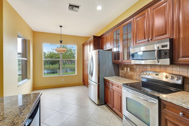 kitchen featuring light tile patterned floors, appliances with stainless steel finishes, light stone counters, tasteful backsplash, and decorative light fixtures