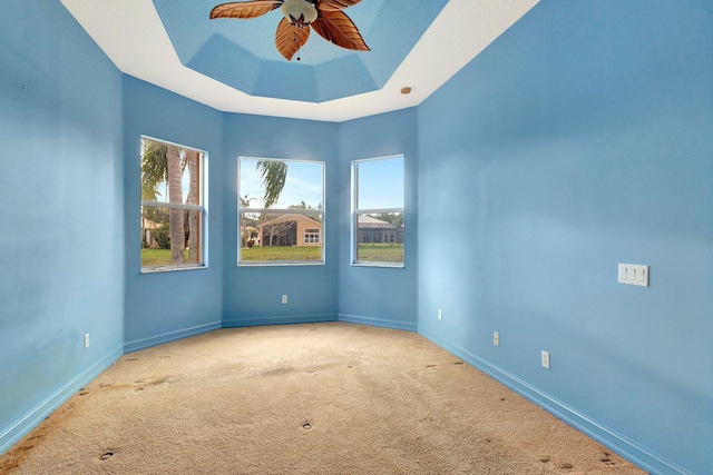 spare room featuring light carpet, a tray ceiling, and ceiling fan