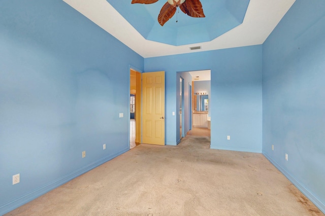 spare room with a raised ceiling, light colored carpet, and ceiling fan