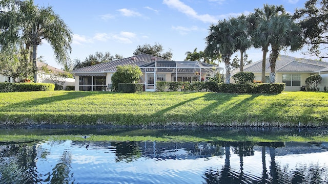 back of property with a water view, glass enclosure, and a lawn