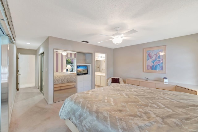 bedroom with ceiling fan, light colored carpet, ensuite bath, and a textured ceiling