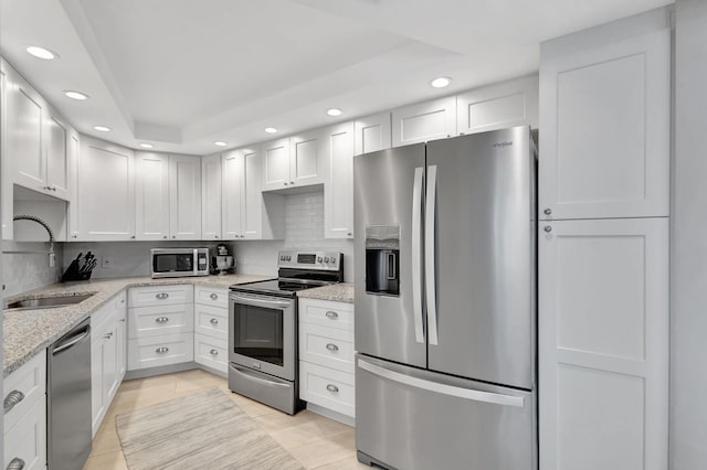 kitchen with white cabinets, appliances with stainless steel finishes, light stone countertops, and sink