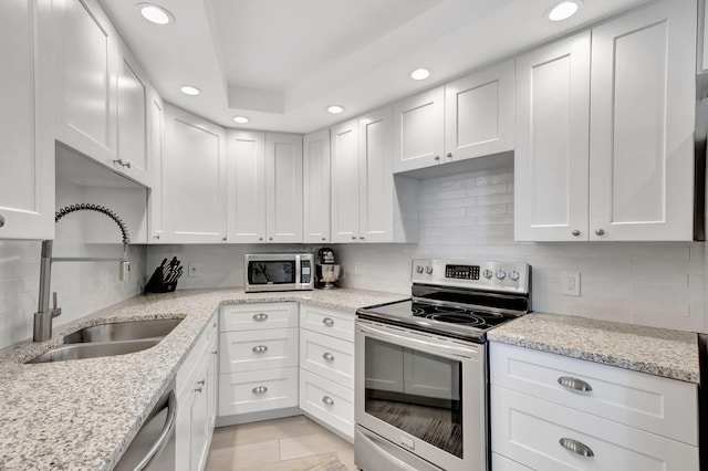 kitchen featuring sink, decorative backsplash, light stone countertops, white cabinetry, and stainless steel appliances