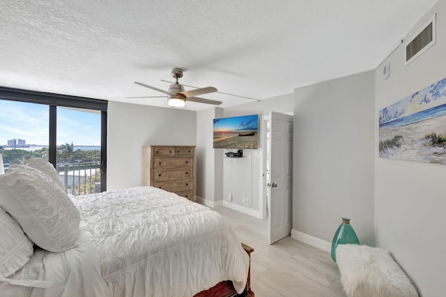 bedroom featuring floor to ceiling windows, ceiling fan, access to exterior, a textured ceiling, and light hardwood / wood-style floors