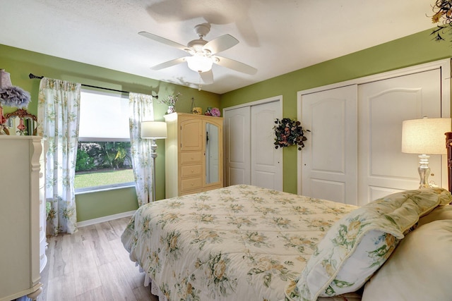 bedroom with light wood-style floors, baseboards, a ceiling fan, and two closets