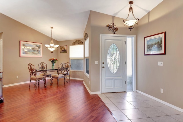 entryway featuring a chandelier, baseboards, vaulted ceiling, and light wood finished floors