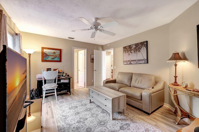 living room featuring light wood finished floors, visible vents, baseboards, a ceiling fan, and a textured ceiling