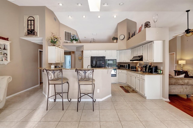 kitchen with black appliances, light tile patterned floors, under cabinet range hood, and a breakfast bar