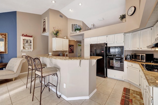 kitchen featuring light tile patterned floors, a peninsula, a breakfast bar, light stone countertops, and black appliances