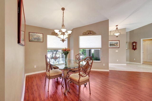 dining space featuring light wood-type flooring, baseboards, vaulted ceiling, and a notable chandelier