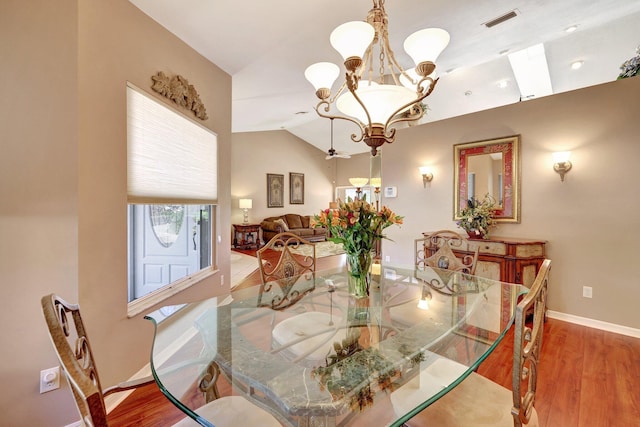 dining room with a chandelier, wood finished floors, visible vents, baseboards, and vaulted ceiling