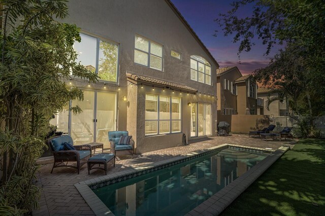 back house at dusk with a fenced in pool, an outdoor hangout area, and a patio