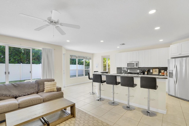 kitchen featuring appliances with stainless steel finishes, light tile patterned floors, white cabinets, a breakfast bar area, and an island with sink