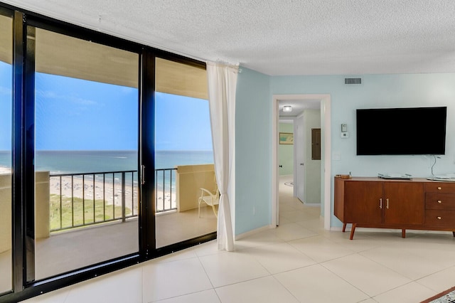 unfurnished living room featuring a textured ceiling, light tile patterned flooring, a view of the beach, and a wall of windows