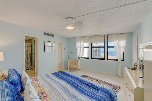 tiled bedroom with a textured ceiling, ceiling fan, and connected bathroom