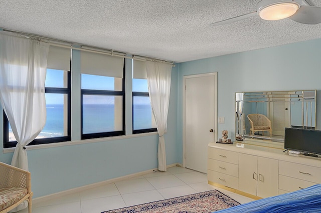 unfurnished bedroom with ceiling fan, a water view, a textured ceiling, and multiple windows