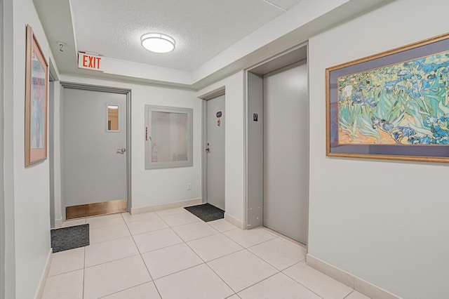 hallway with light tile patterned floors, a textured ceiling, and elevator