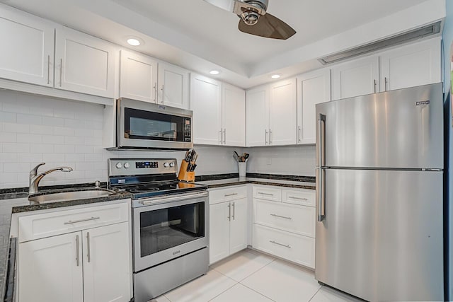 kitchen with decorative backsplash, dark stone counters, stainless steel appliances, sink, and white cabinets